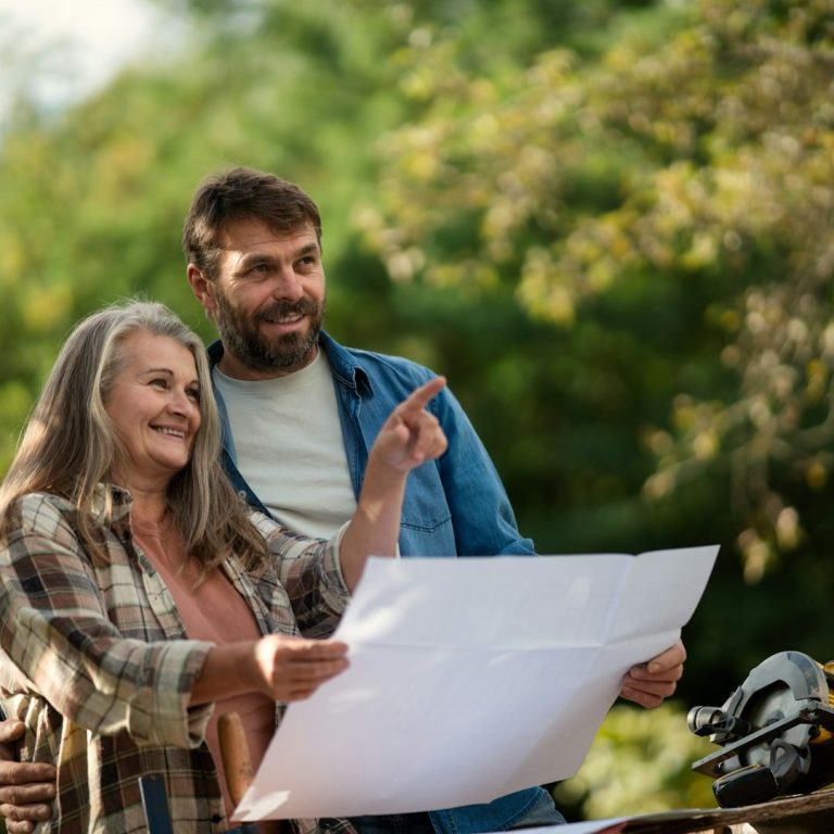 Planung vor Ort Zwei Personen betrachten einen Plan im Freien und lächeln sich an.